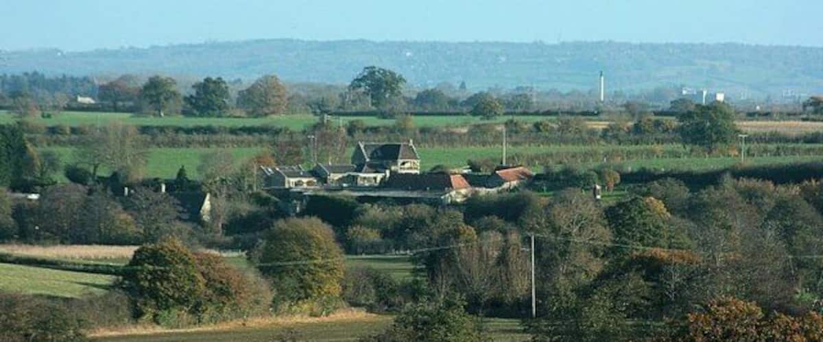A rural landscape with rolling hills, scattered houses, and a clear sky.