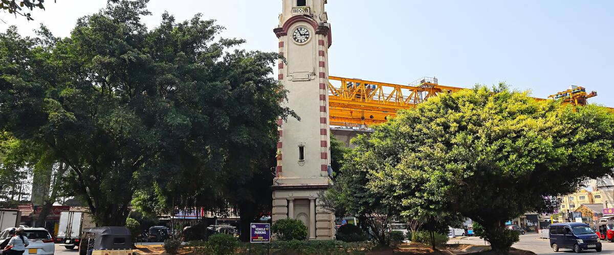 A clock tower, a crane, and a busy street with vehicles and trees.