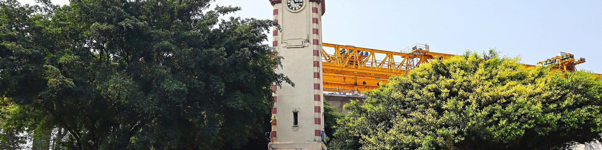 A clock tower, a crane, and a busy street with vehicles and trees.