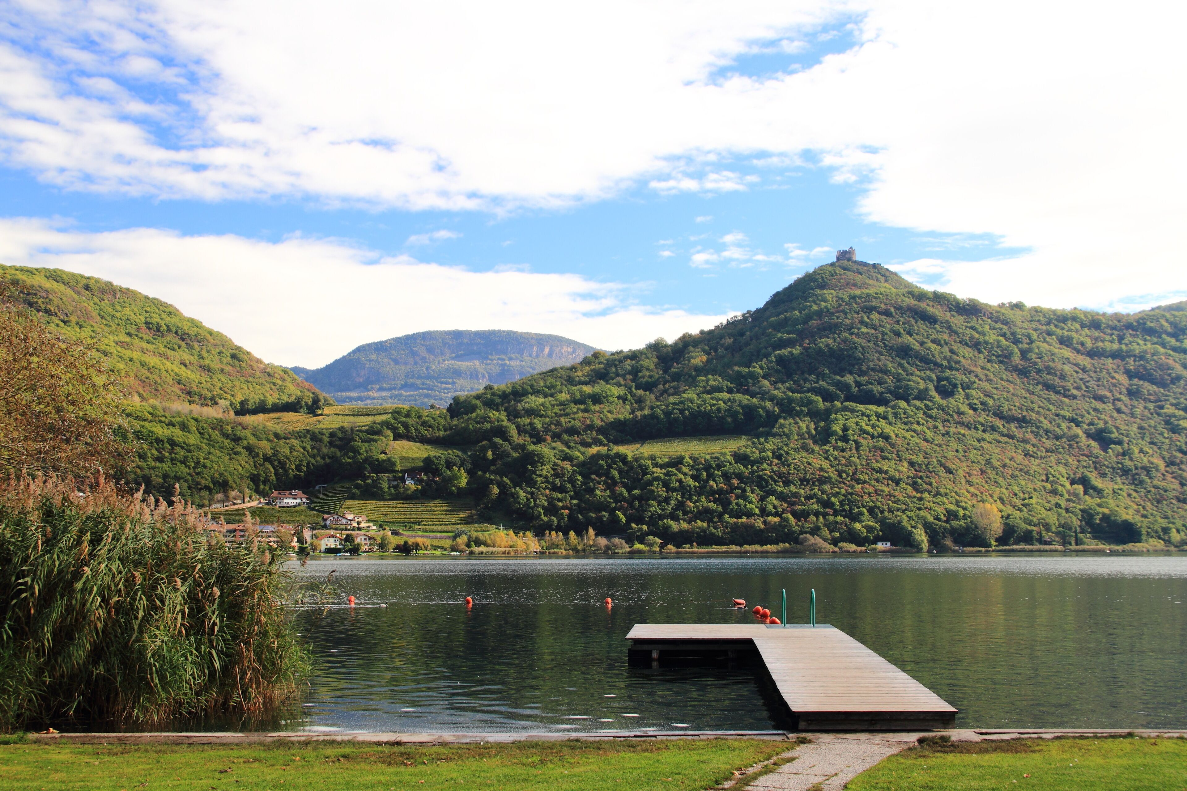 A lake surrounded by hills, a wooden dock, and a distant castle-like structure.