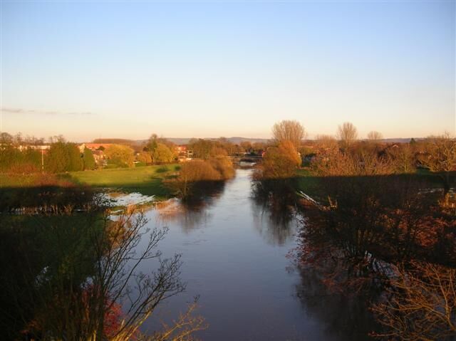 A calm river with trees and a distant town.