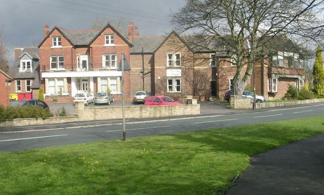 A residential street with houses, parked cars, and a grassy area.