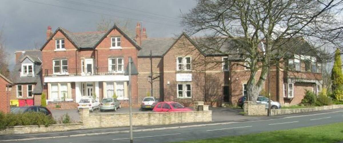 A residential street with houses, parked cars, and a grassy area.