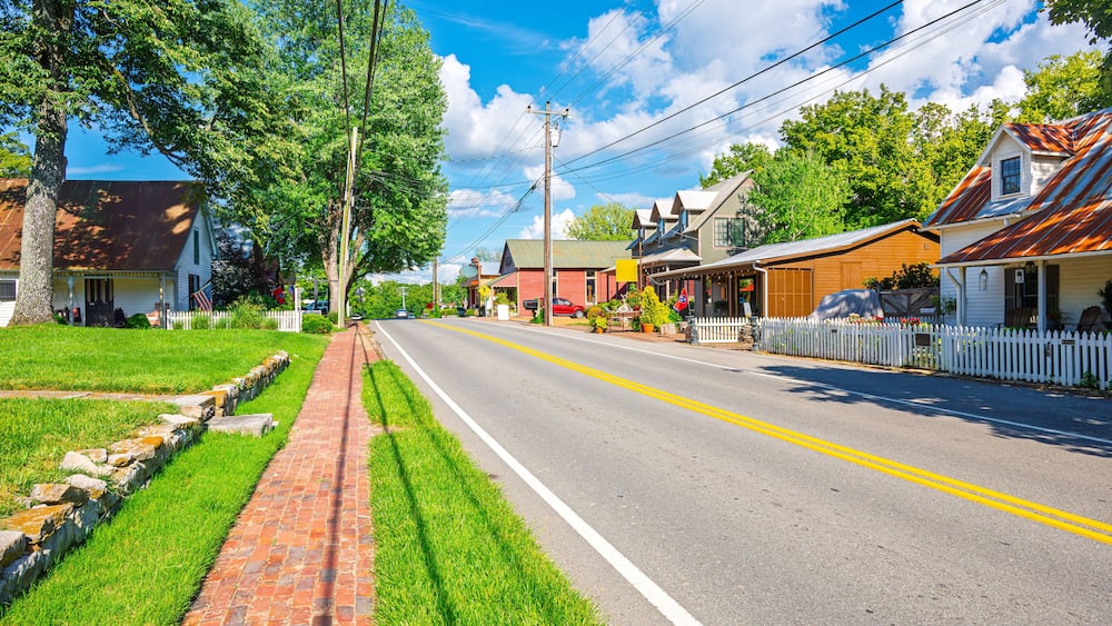A sunny street lined with houses, a brick sidewalk, and a white picket fence.