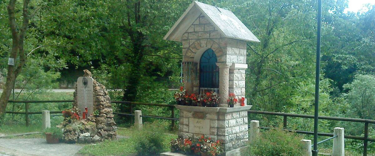 A stone structure with a blue door, surrounded by flowers and greenery.