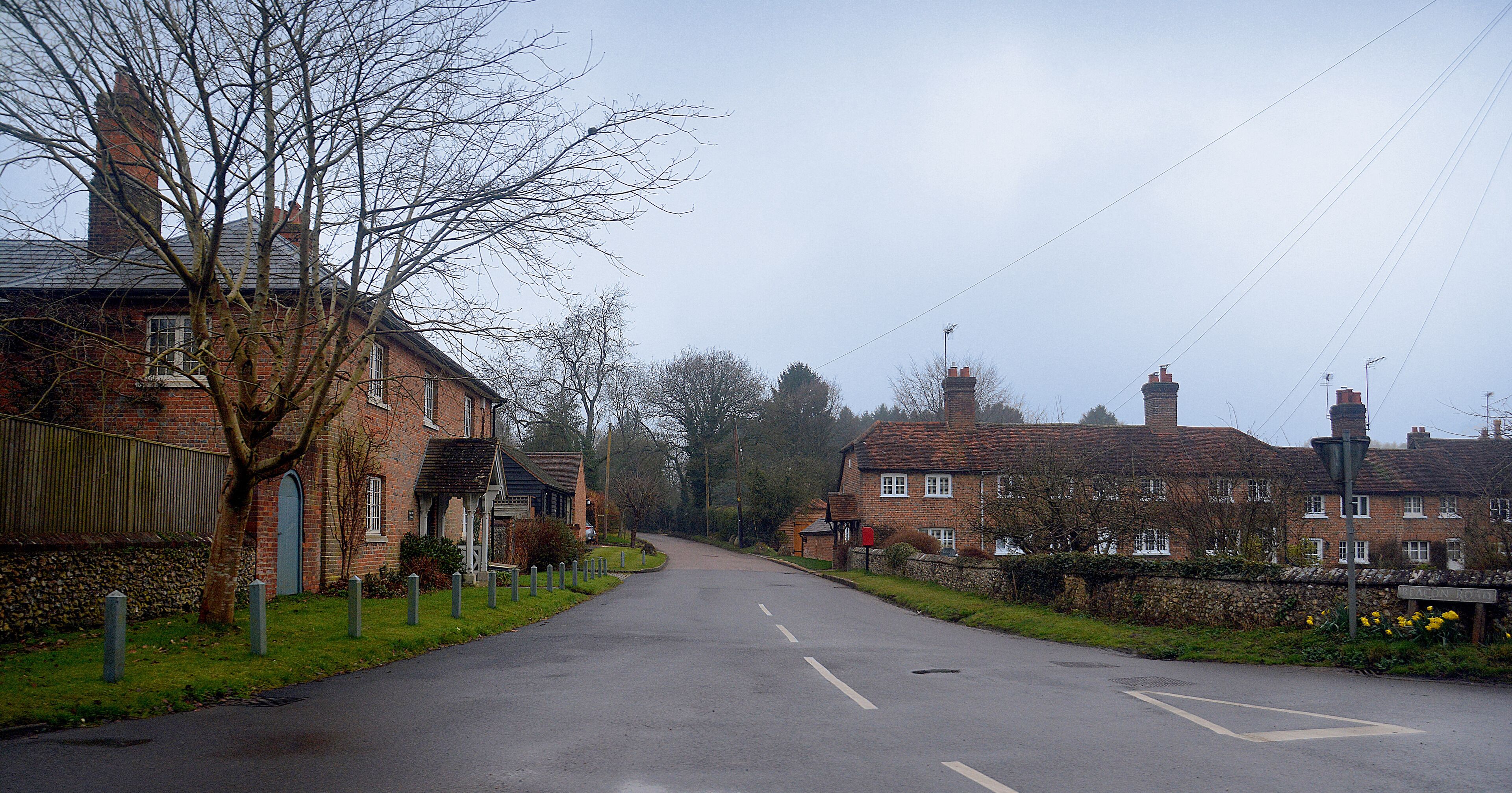 A quiet rural road flanked by traditional brick houses and a stone wall.