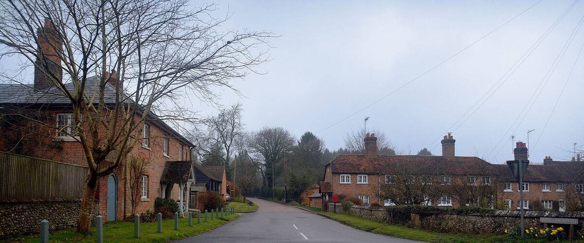 A quiet rural road flanked by traditional brick houses and a stone wall.