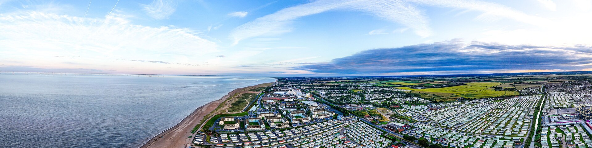 An aerial view of a coastal area with a beach, a marina, and a large caravan park.
