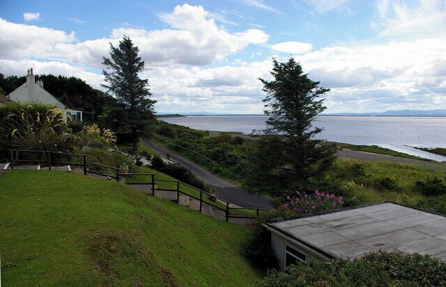 A coastal landscape with a grassy hill, a wooden staircase, and a view of the sea.