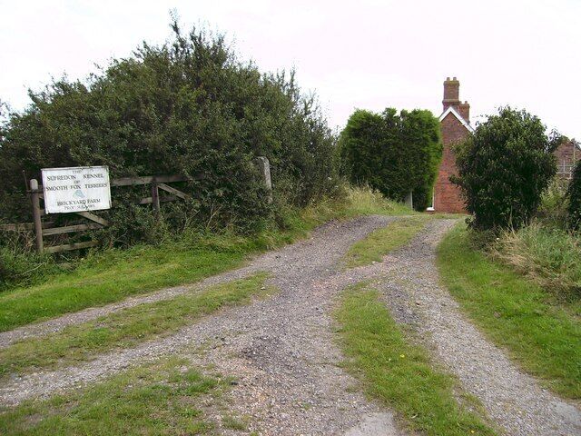 A gravel path leading to a brick building with a signboard.