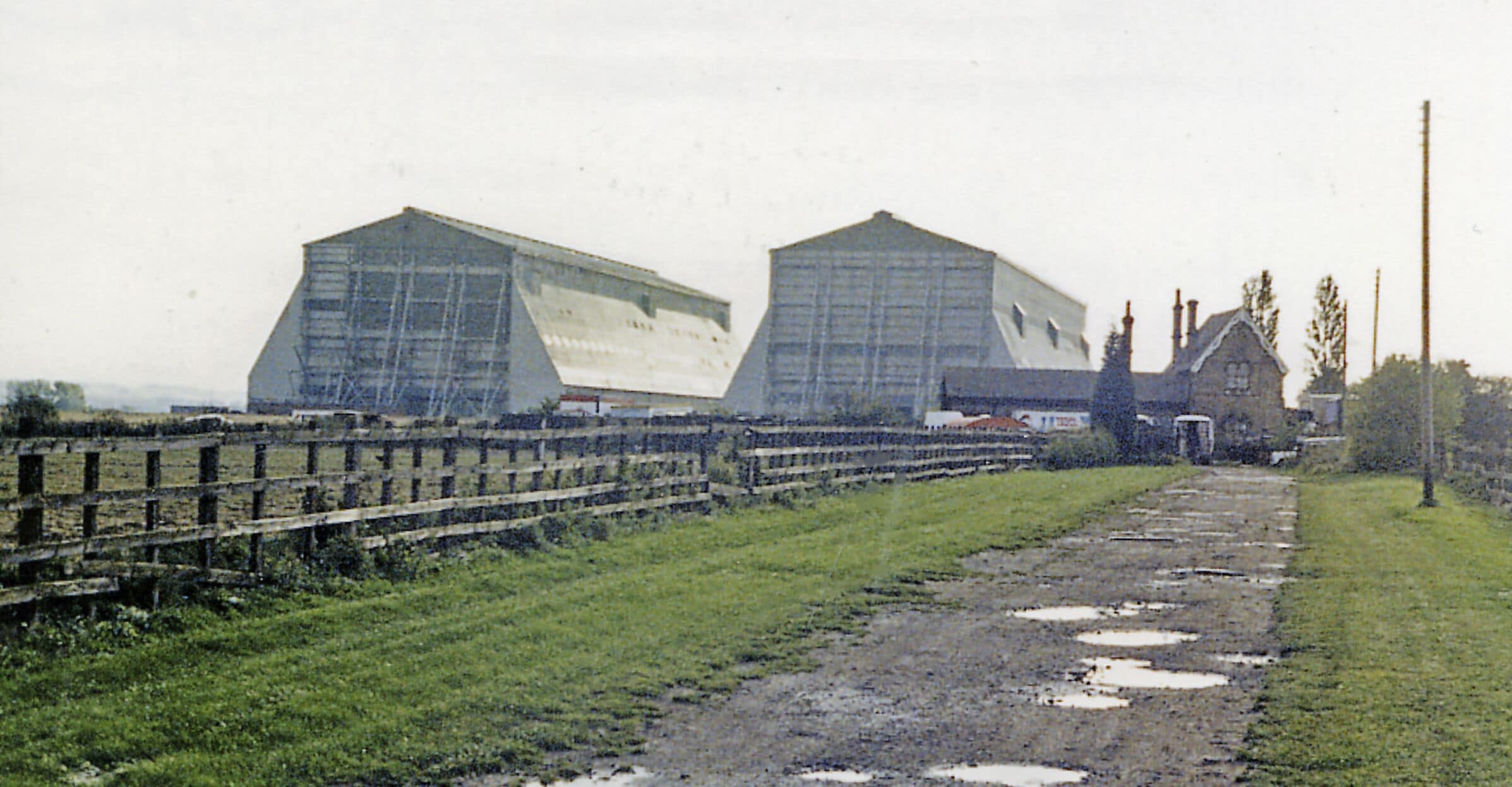 Cardington station (remains) and Airship Sheds, 1987. View SW, across the former ex-Midland Bedford (right) - Hitchin (left) line. The line was closed to passengers from 1/1/62, but may have remained open for goods until 1969. The station seems to be well preserved, still overshadowed by the Airship Sheds.