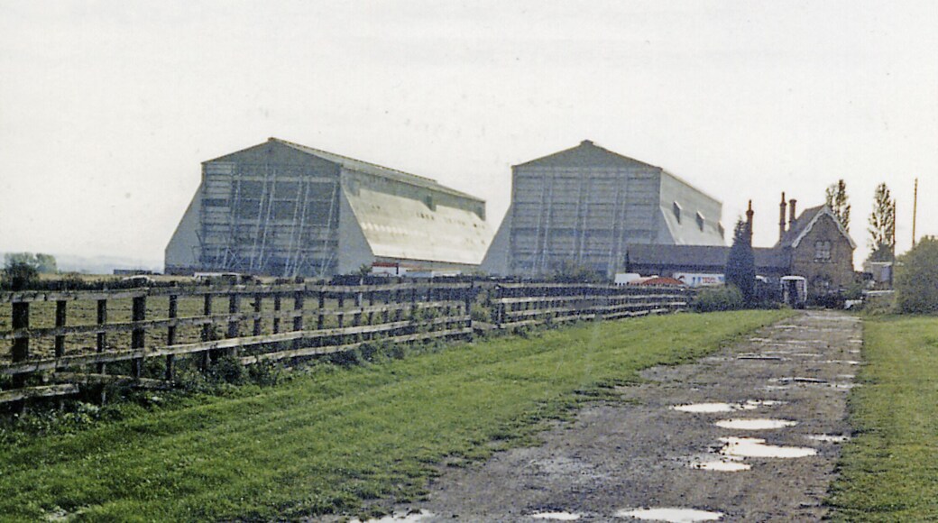 Cardington station (remains) and Airship Sheds, 1987. View SW, across the former ex-Midland Bedford (right) - Hitchin (left) line. The line was closed to passengers from 1/1/62, but may have remained open for goods until 1969. The station seems to be well preserved, still overshadowed by the Airship Sheds.