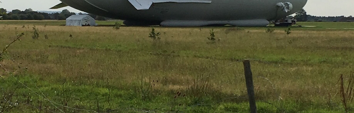 A large blimp with the word "AIRLANDER" on it parked in a grassy field.
