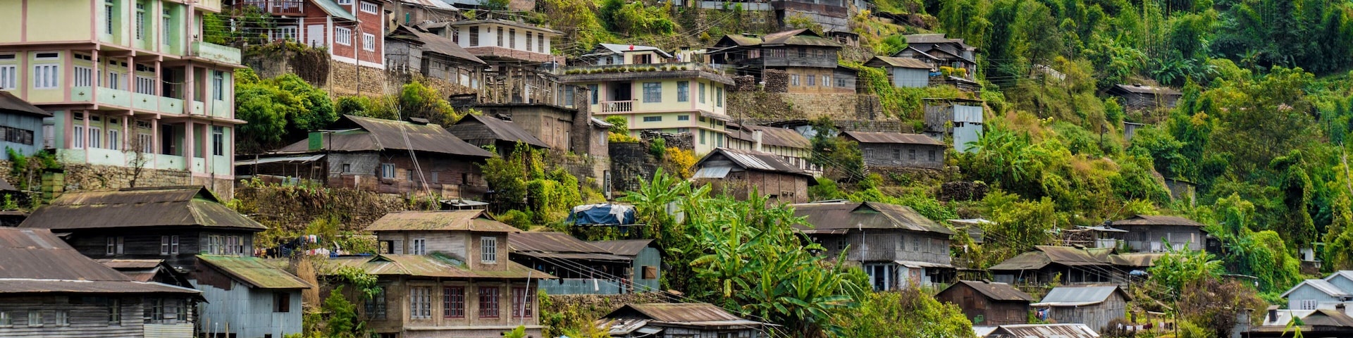 Un pueblo en la ladera con casas tradicionales construidas sobre terreno empinado, rodeado de abundante vegetación.