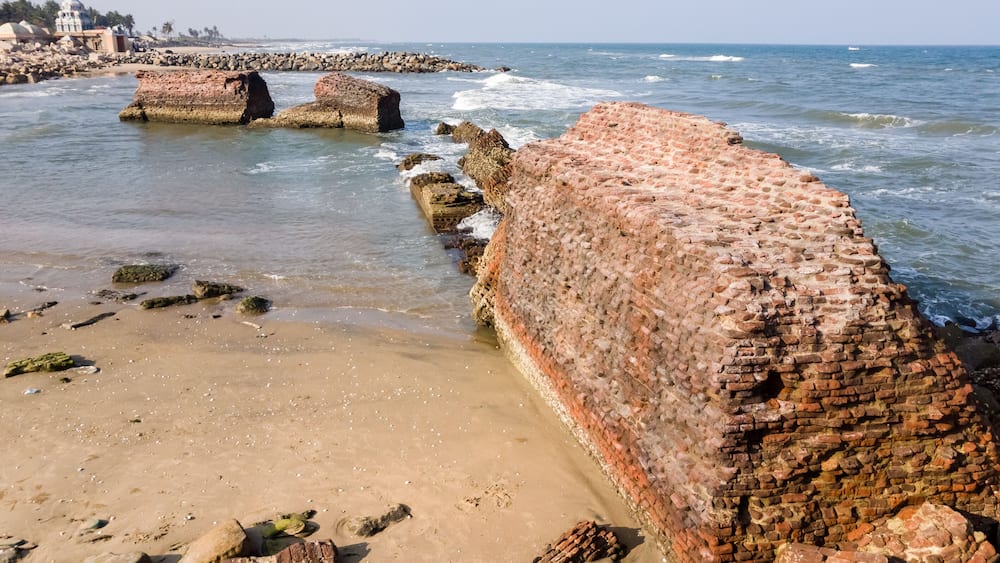 A coastal beach with large, weathered brick walls and scattered rocks.