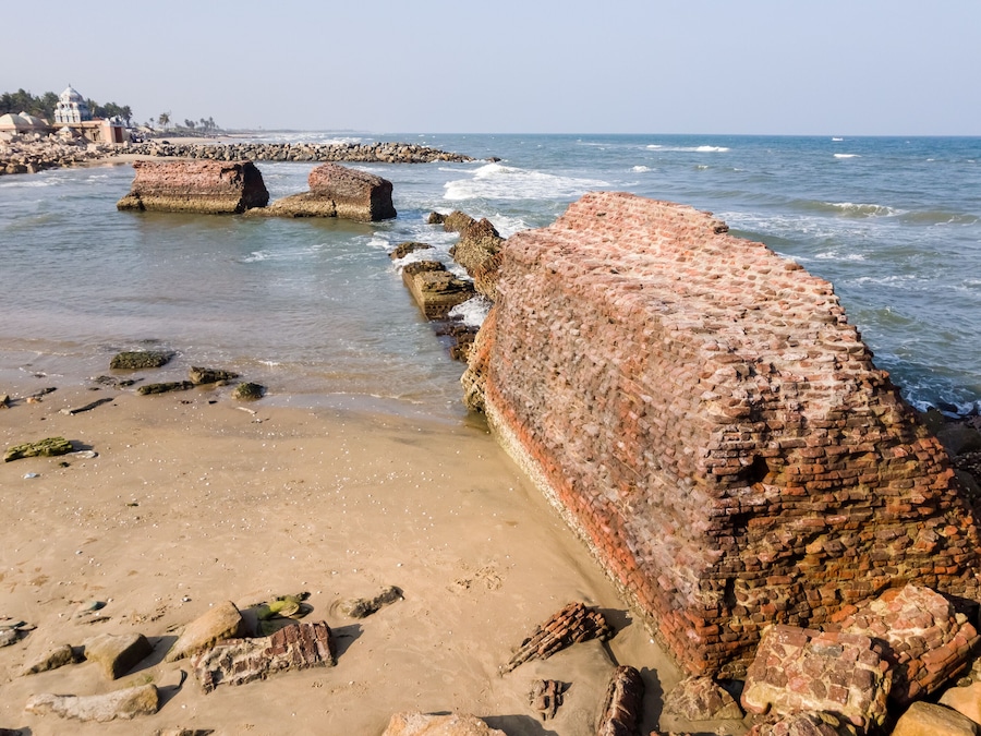 Una playa costera con grandes muros de ladrillo erosionado y rocas dispersas.