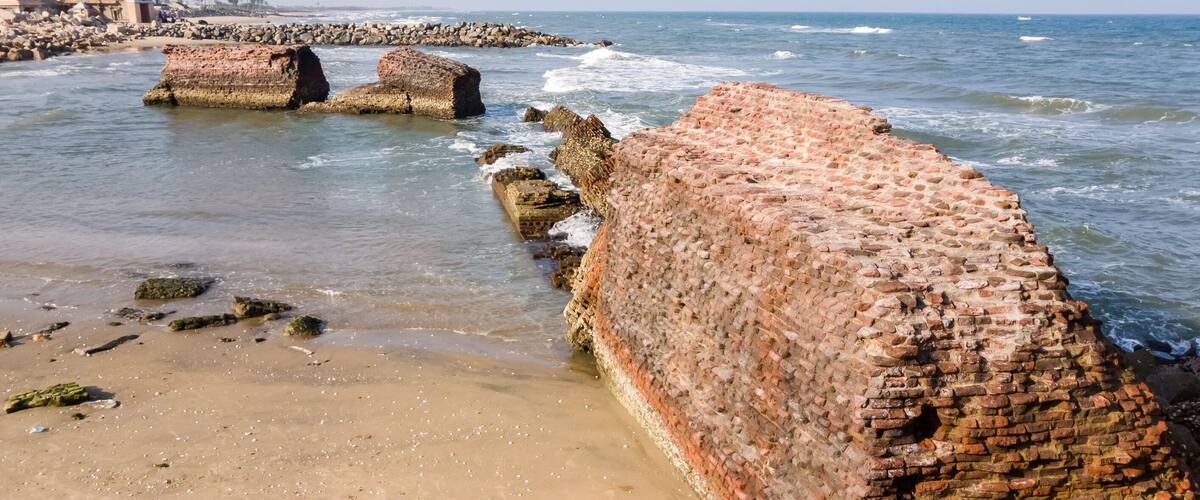 A coastal beach with large, weathered brick walls and scattered rocks.
