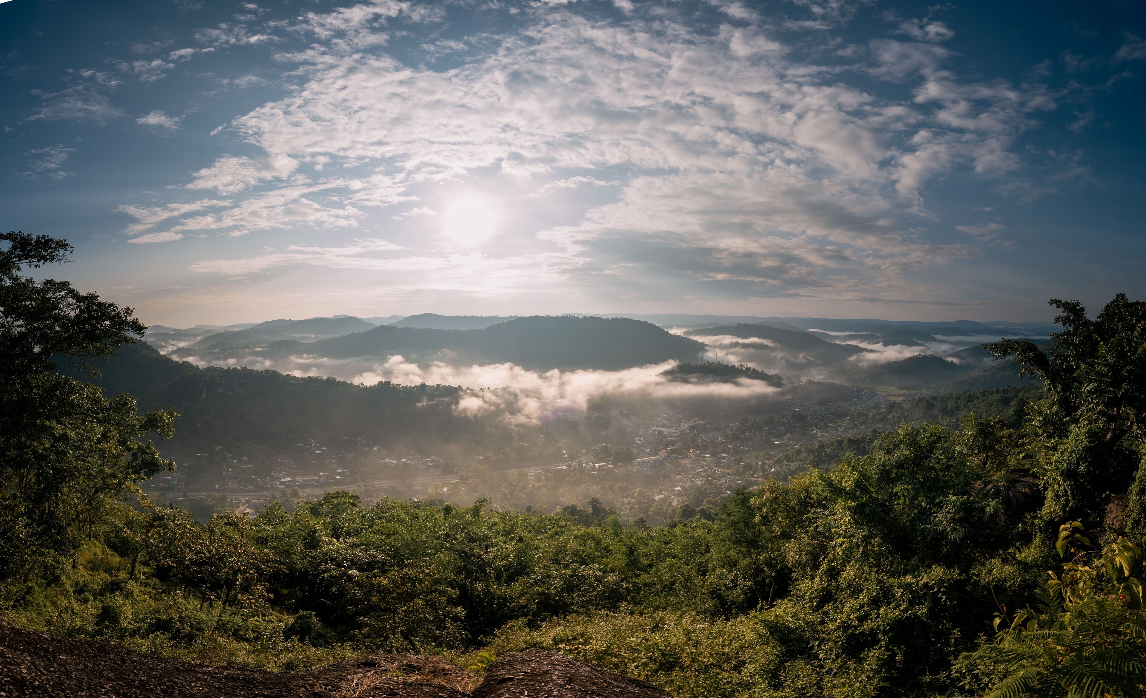 A mountainous landscape with dense forests, a valley, and a sunlit sky.