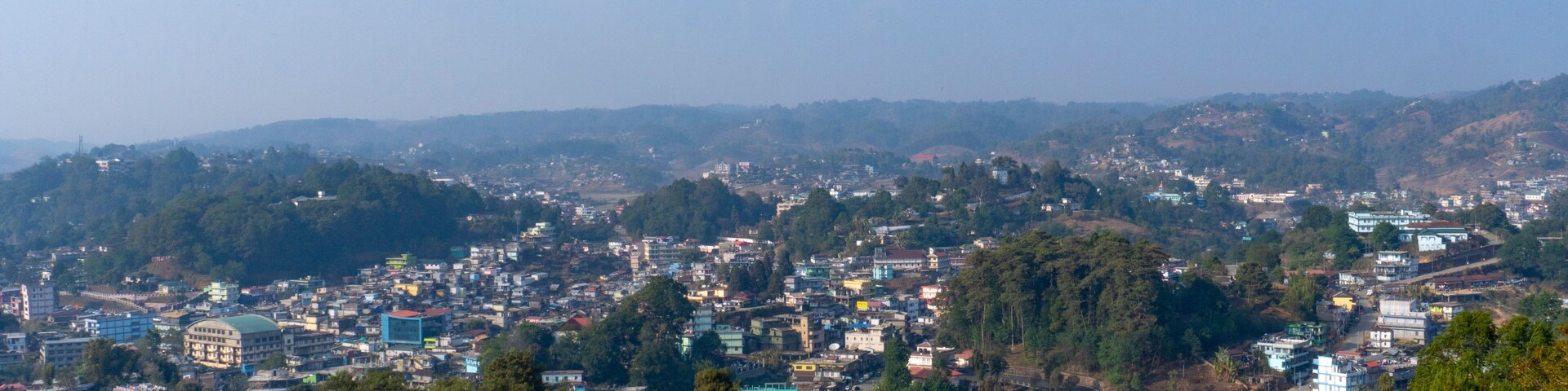 A densely populated cityscape with numerous buildings and a backdrop of hills and trees.
