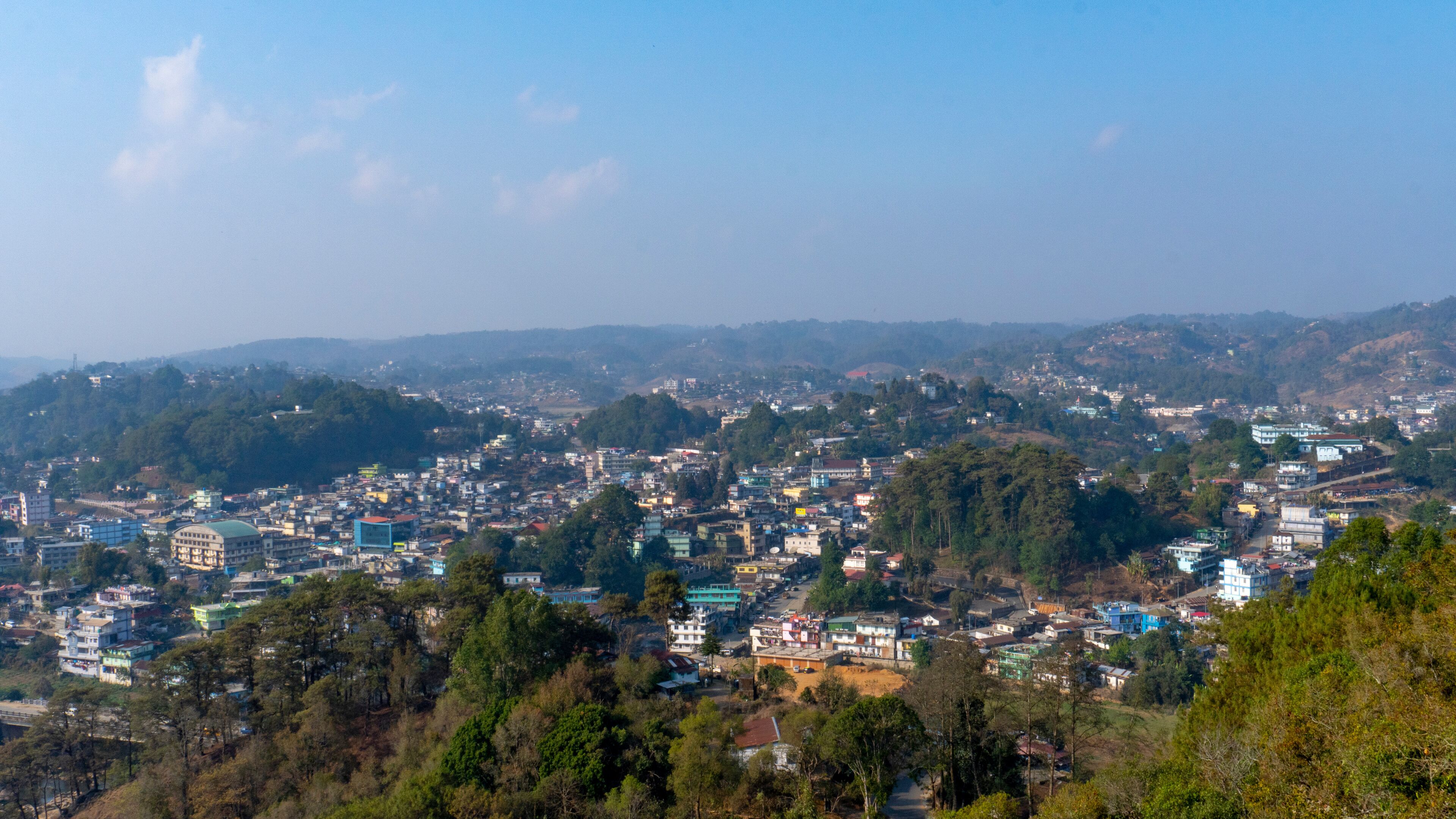 A densely populated cityscape with numerous buildings and a backdrop of hills and trees.