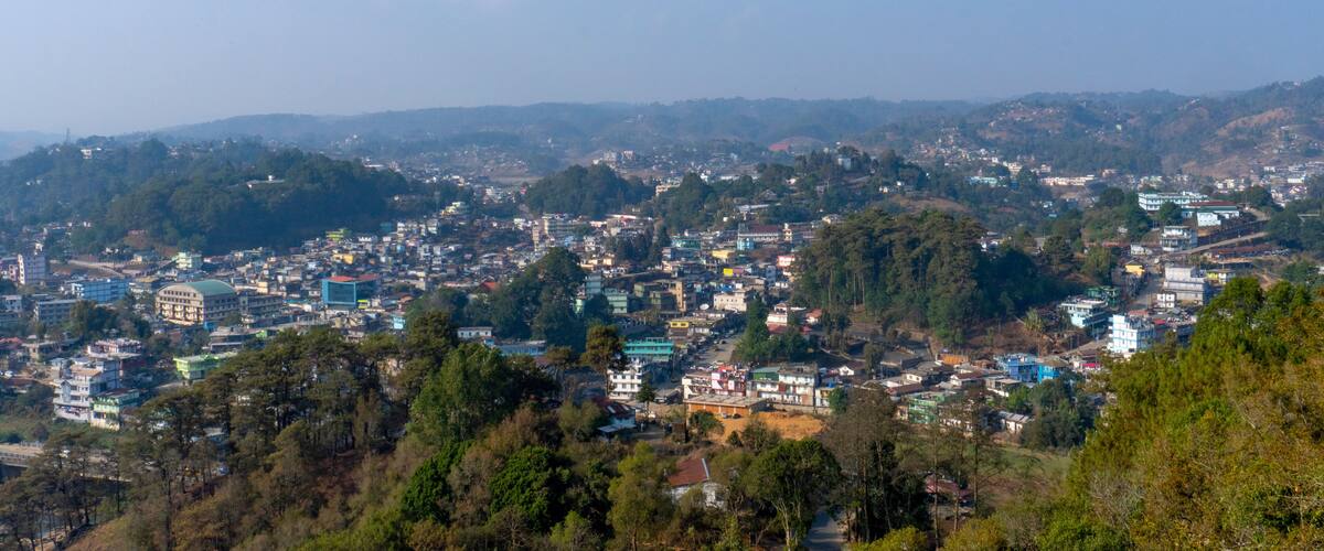 A densely populated cityscape with numerous buildings and a backdrop of hills and trees.