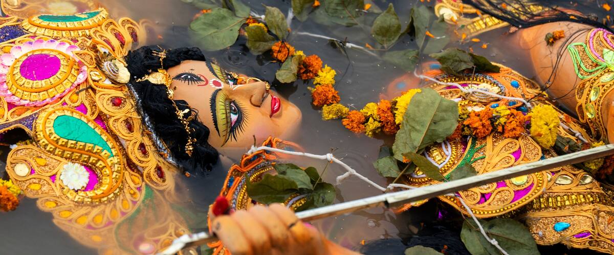 A person in elaborate traditional attire with intricate jewelry and decorations, partially submerged in water with leaves and flowers around.