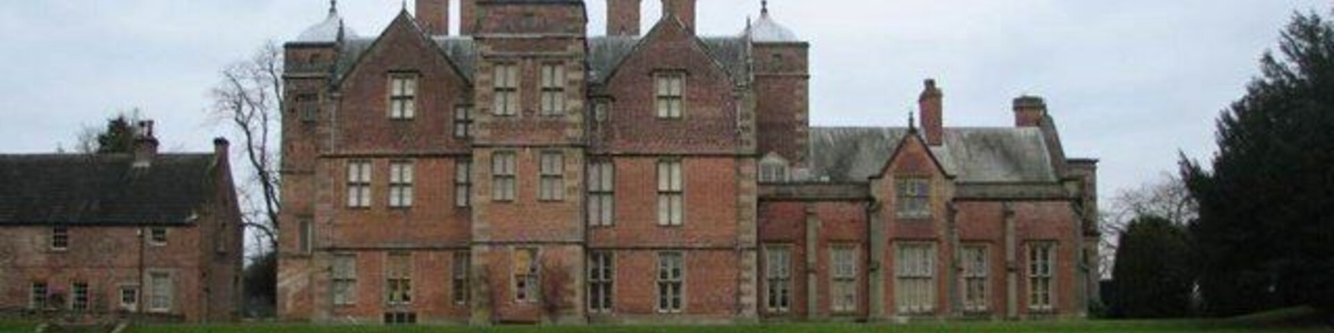 Un edificio grande y de aspecto histórico de ladrillo con múltiples torres y un césped bien cuidado al frente.