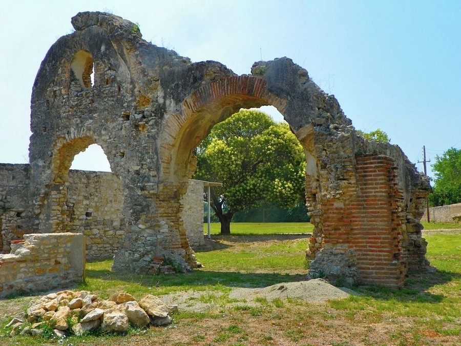 Ruinas de piedra antiguas con un gran arco y un árbol al fondo.