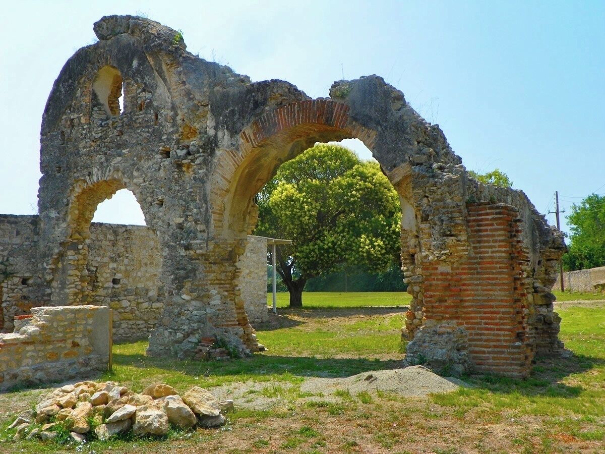 Ancient stone ruins with a large archway and a tree in the background.