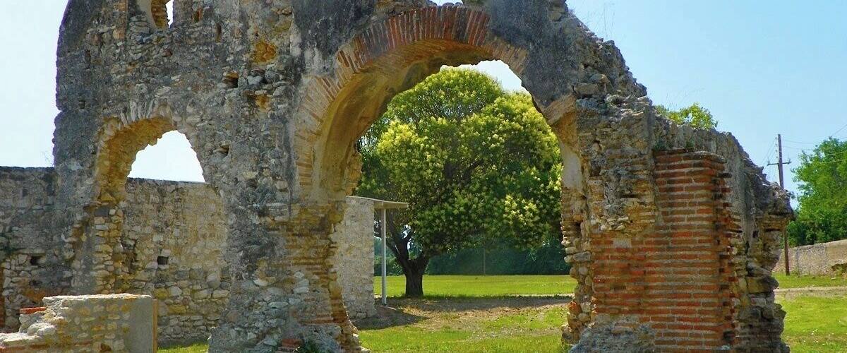 Ancient stone ruins with a large archway and a tree in the background.