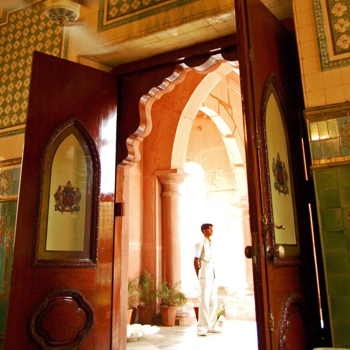 A grand entrance with ornate wooden doors, a person standing in the doorway, and a tiled interior with floral patterns.