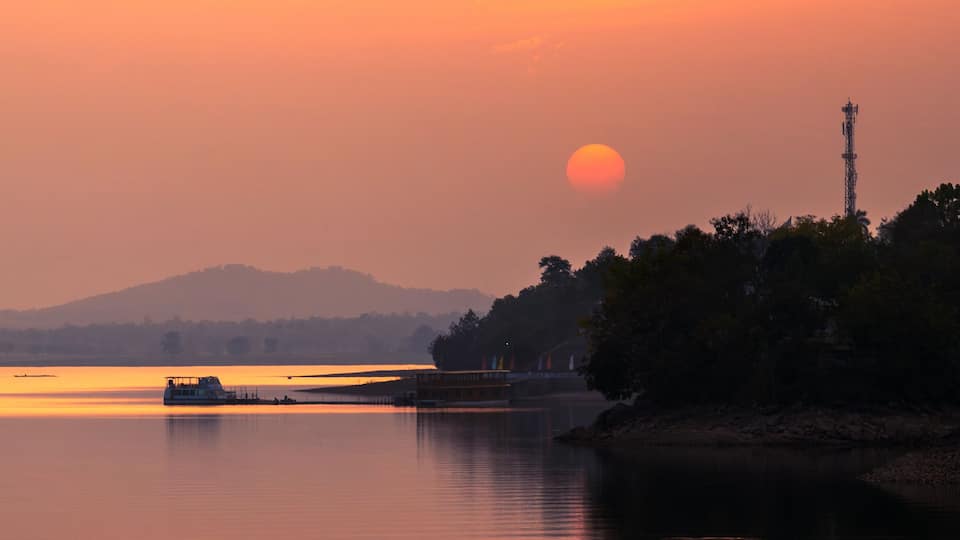 A sunset over a calm lake with a boat and a communication tower in the background.