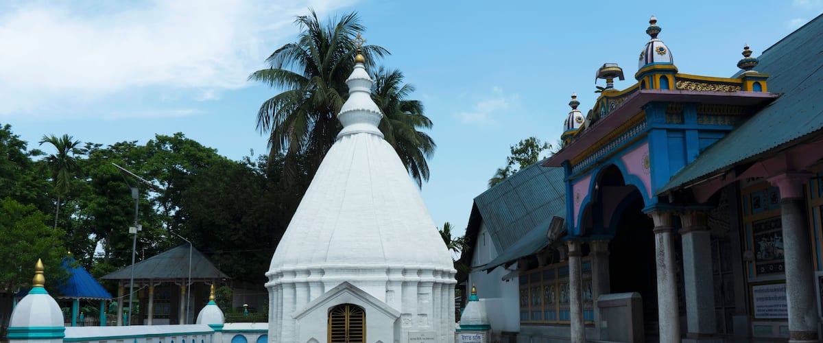 A white temple with a golden door, surrounded by a blue and white fence, and palm trees in the background.