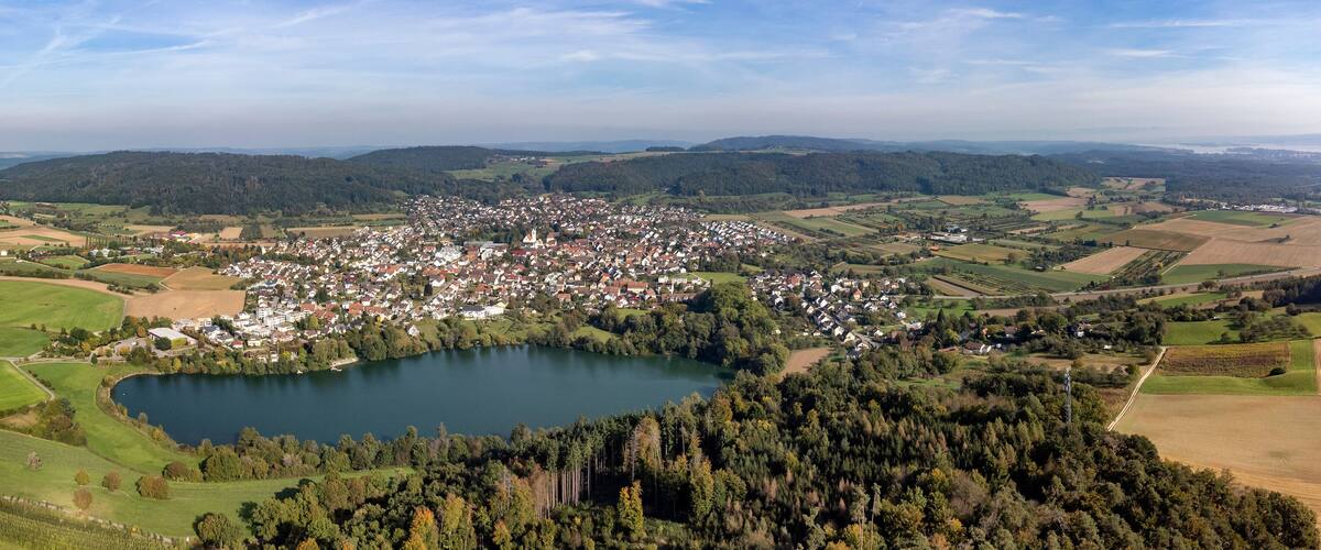 A town surrounded by fields, a lake, and forested hills.