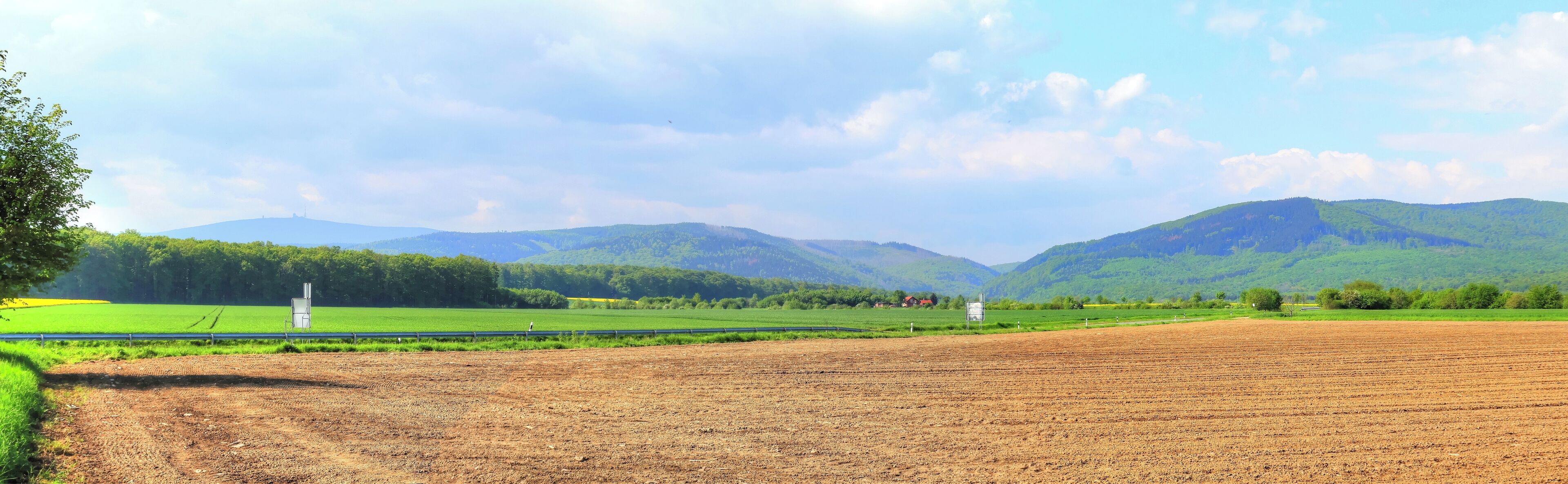 A rural landscape with fields, a fence, and mountains in the background.