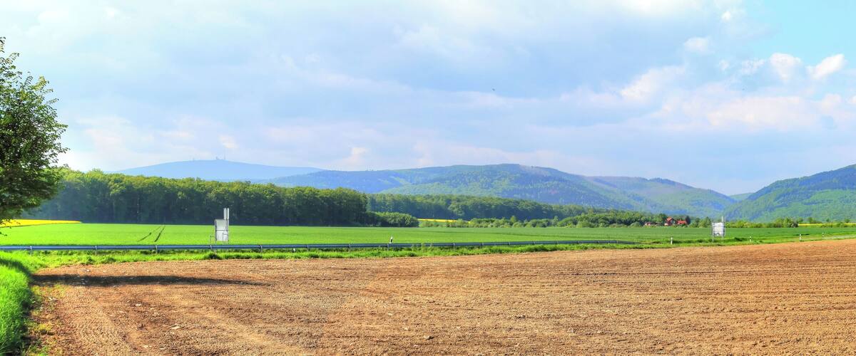 A rural landscape with fields, a fence, and mountains in the background.