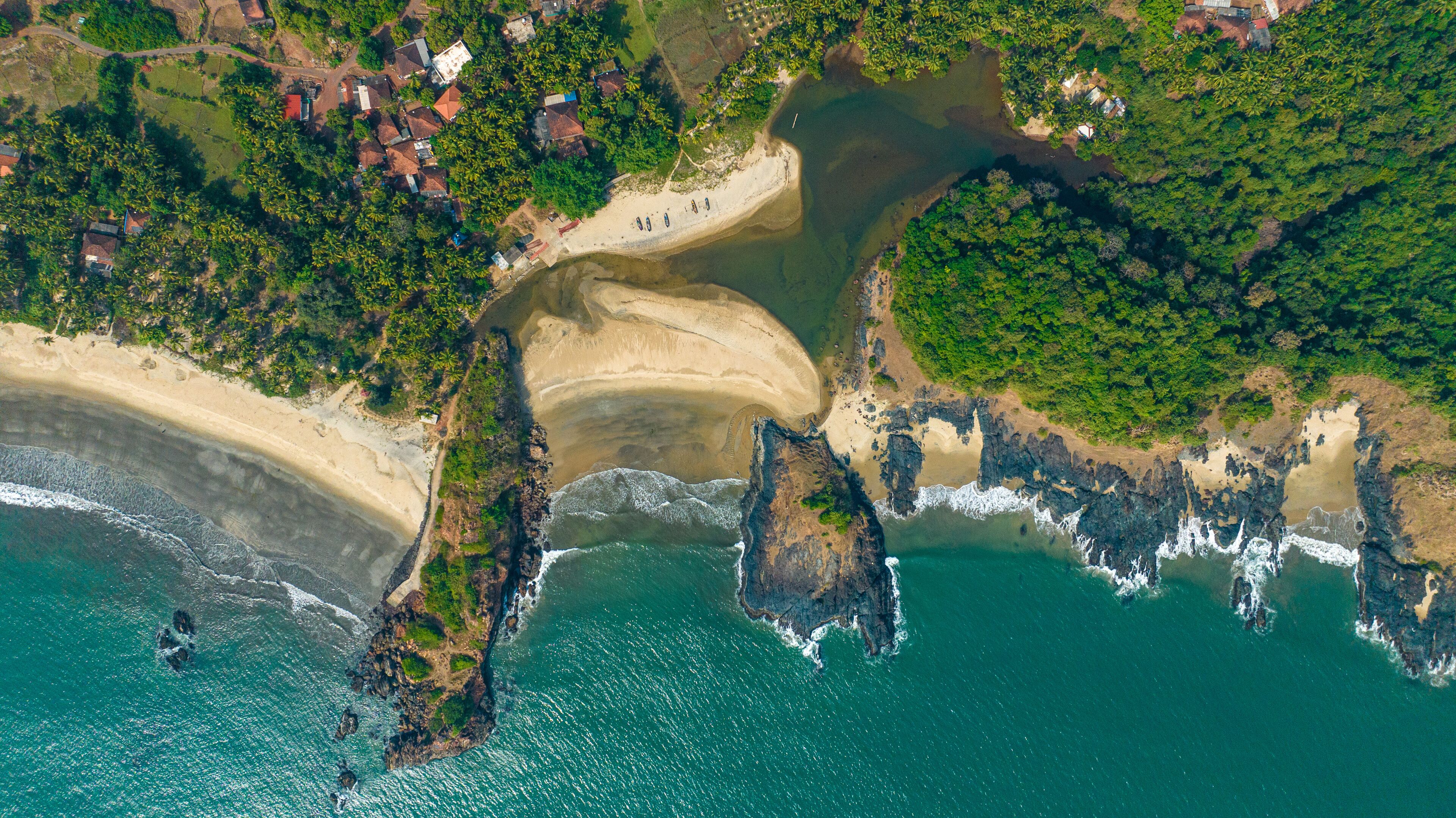 An aerial view of a coastal area with a sandy beach, rocky outcrops, and dense greenery.