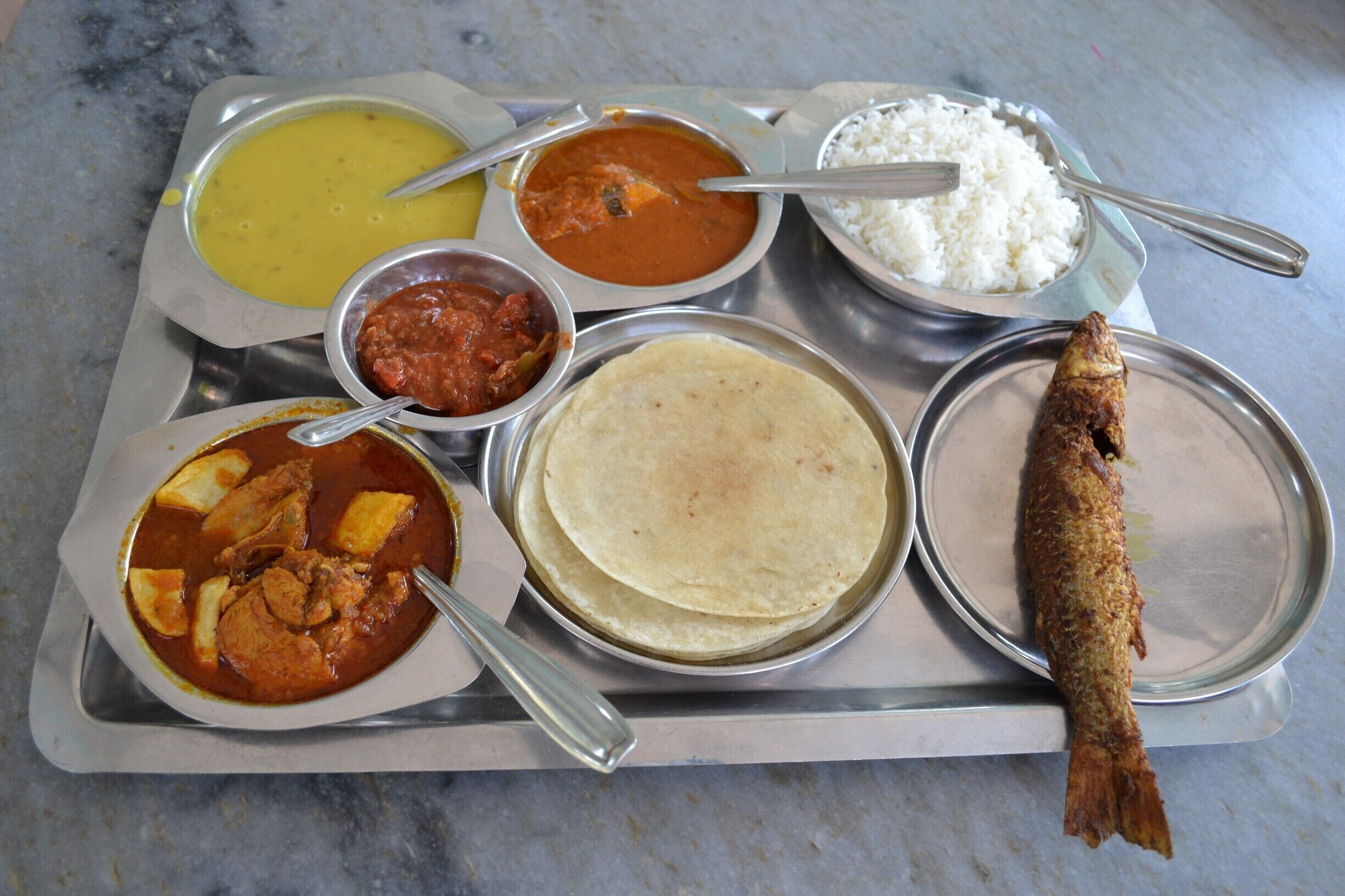 A meal tray with various dishes including curry, rice, a fish, and a flatbread.