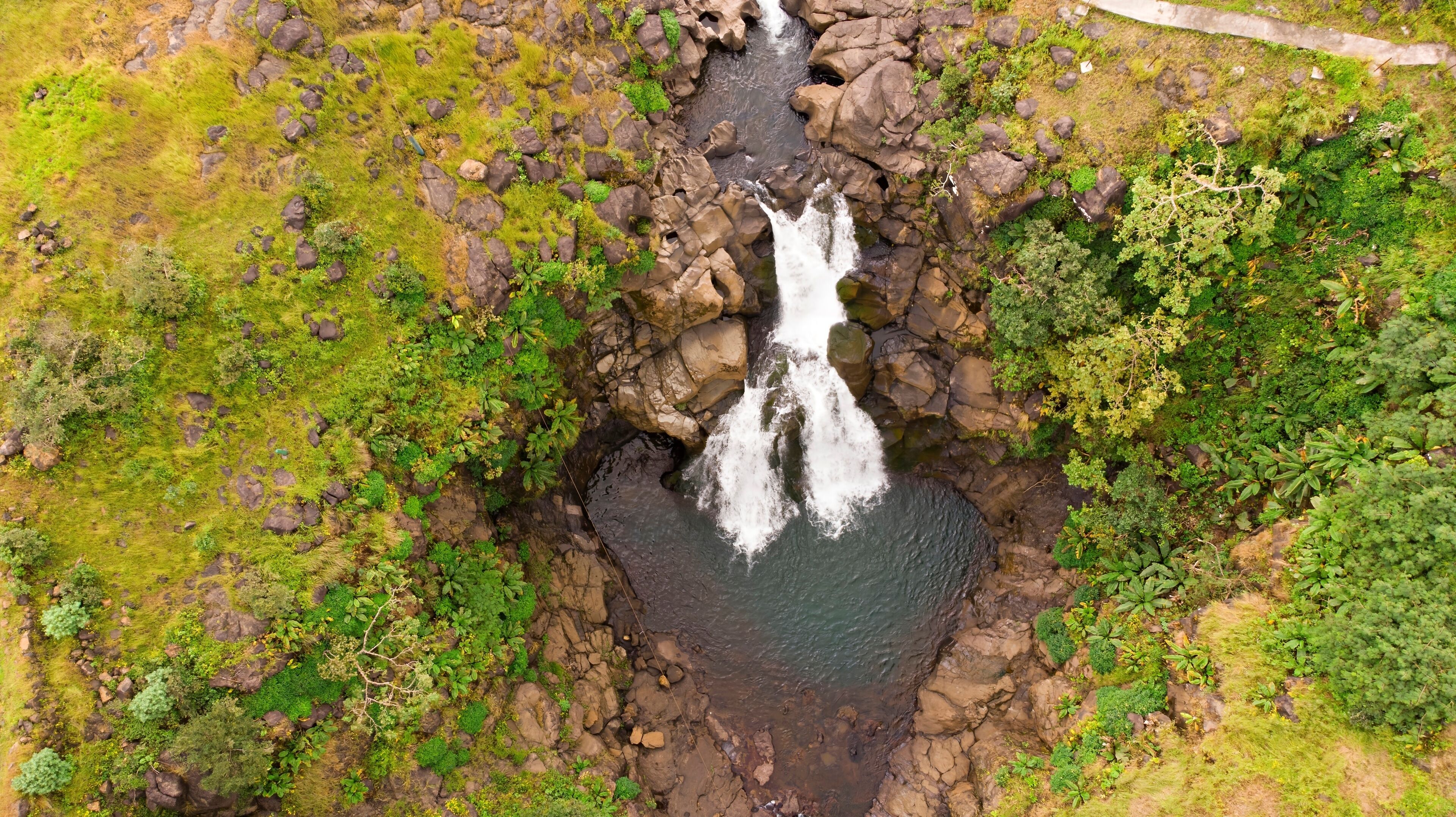 An aerial view of a waterfall surrounded by lush greenery and rocky terrain.