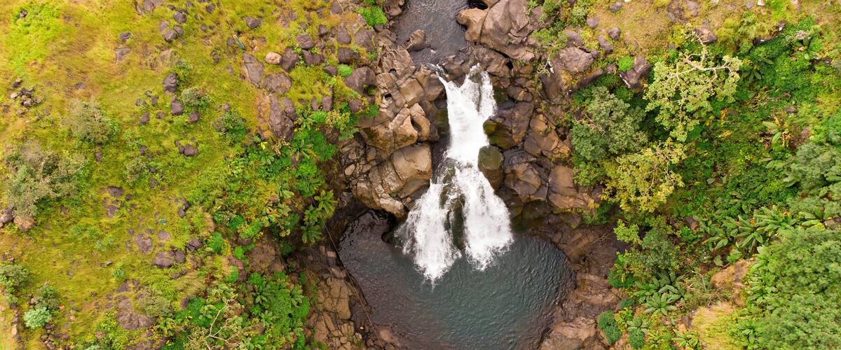 An aerial view of a waterfall surrounded by lush greenery and rocky terrain.