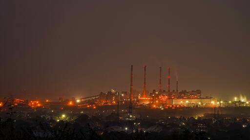 Night urban landscape with an industrial complex with its metal structures and chimneys with reflection of lamps with yellow lights of the city.