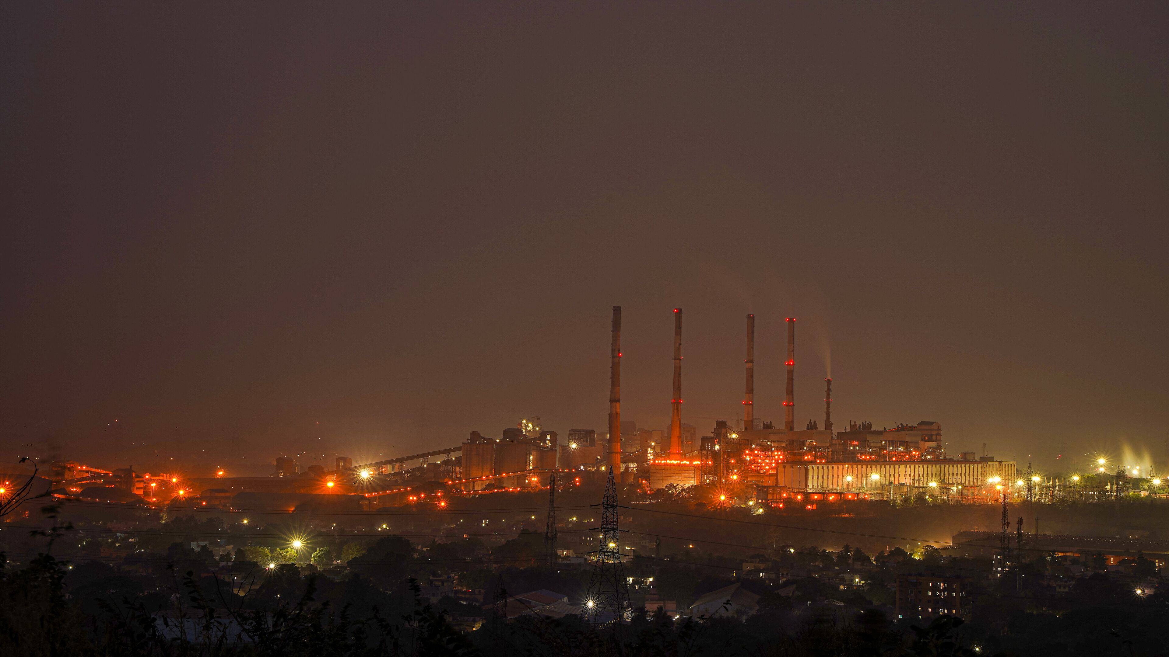 A large industrial complex with multiple tall chimneys and extensive lighting at night.