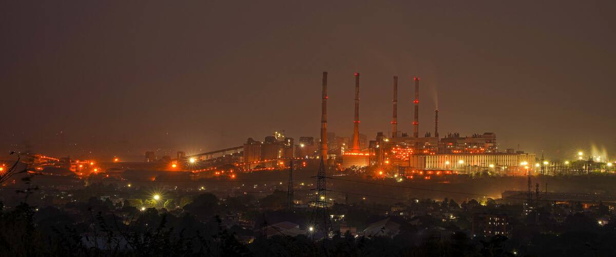 A large industrial complex with multiple tall chimneys and extensive lighting at night.