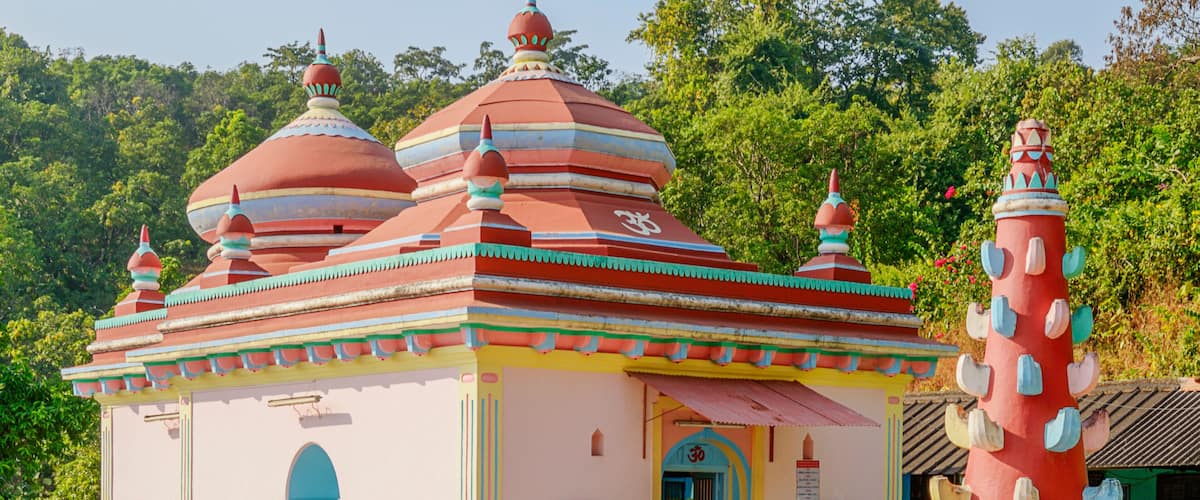 A colorful temple with domed roofs and a large red pillar.