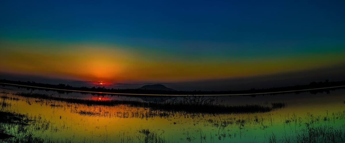 A sunset over a calm lake with a reflection of the sky, surrounded by marshland.