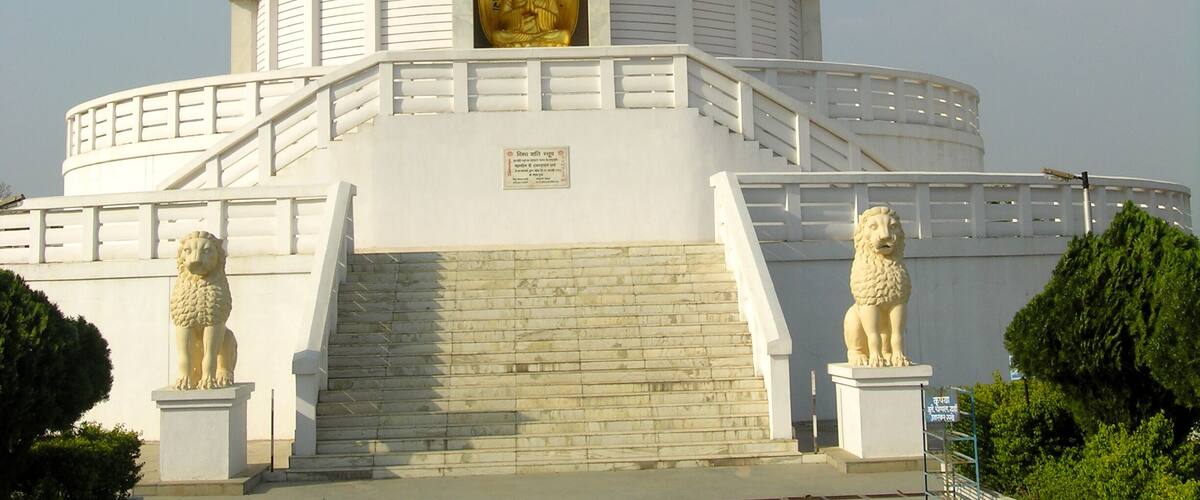 A white stupa with a golden spire, flanked by lion statues, and a staircase leading up to it.