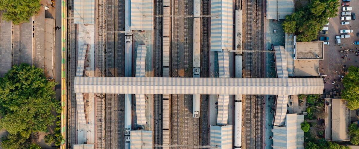 An aerial view of a railway station with multiple tracks and a pedestrian bridge.