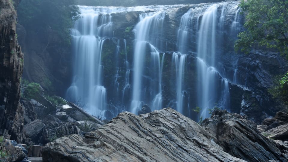 A multi-tiered waterfall surrounded by rocky terrain and greenery.
