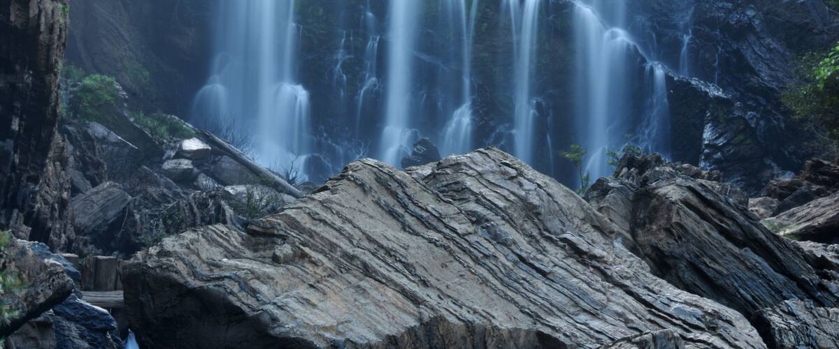 A multi-tiered waterfall surrounded by rocky terrain and greenery.