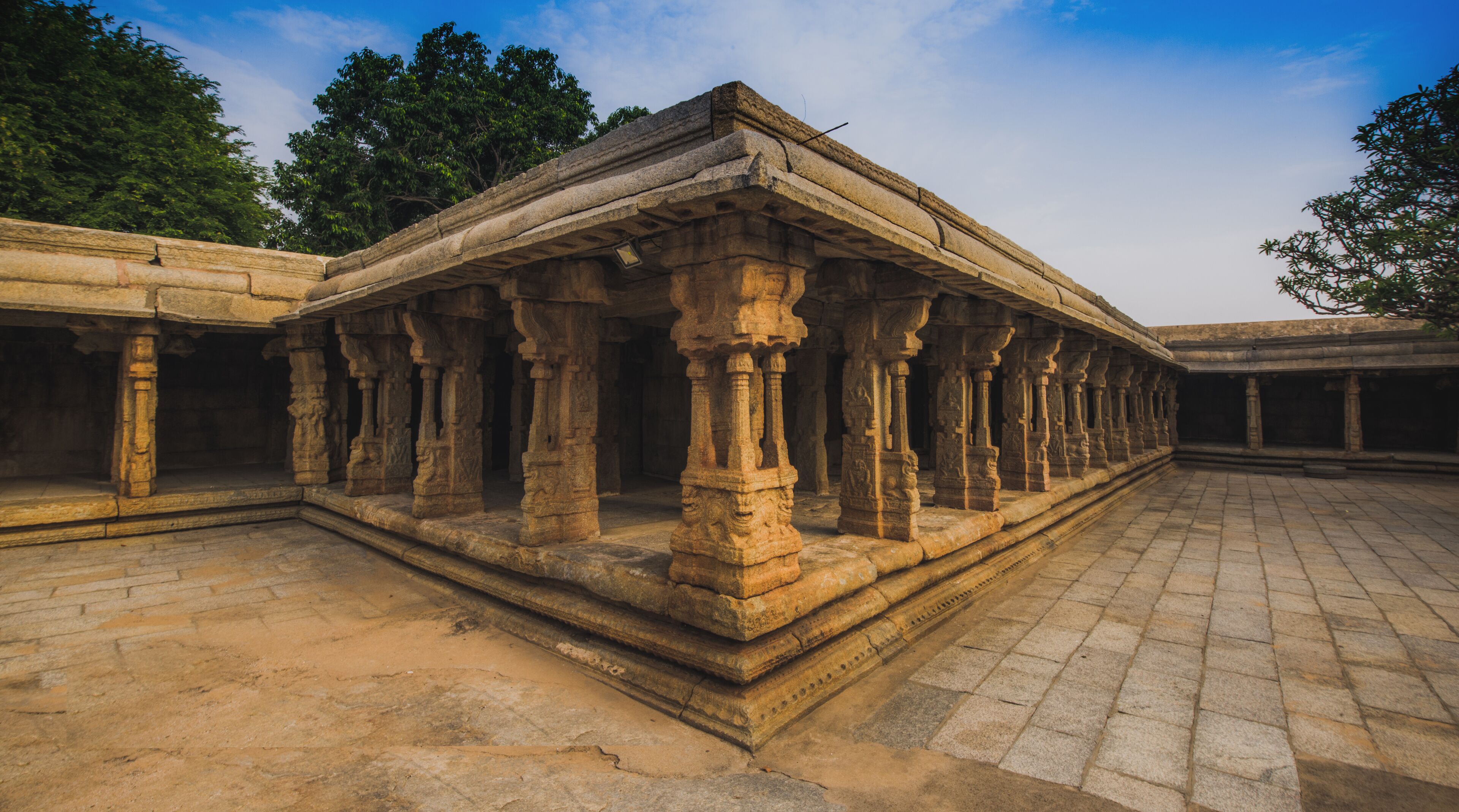 An ancient stone structure with columns and a flat roof, surrounded by trees and a clear sky.